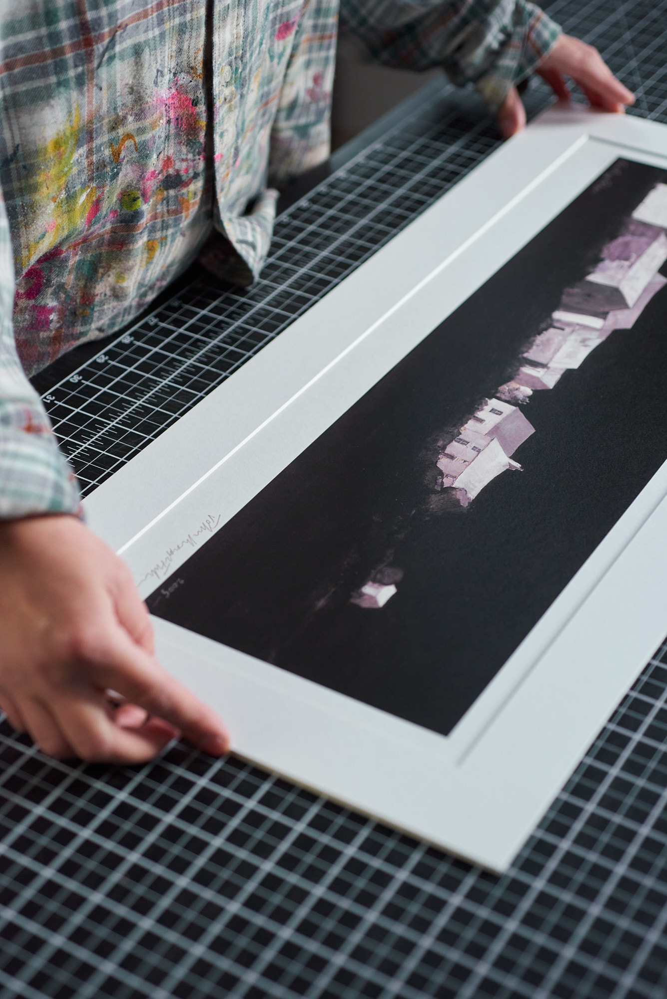 figure wearing checked shirt guiding window mount onto art print on top of black cutting mat